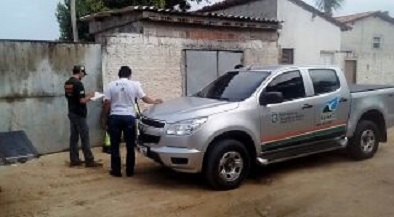 Fotografia de um carro da Semace em frente a um dos locais autuados. Ao lado do carro estão um fiscal folheando alguns papéis e um homem de blusa branca