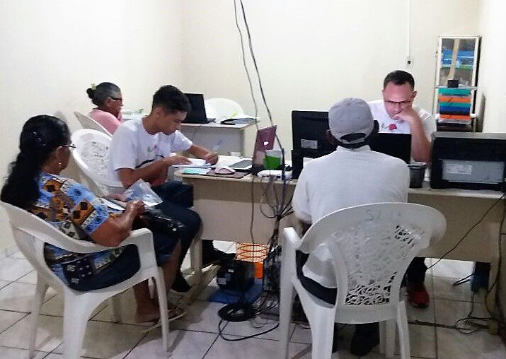 Proprietários rurais em torno de uma mesa com computador. Atendente faz o cadastramento. 