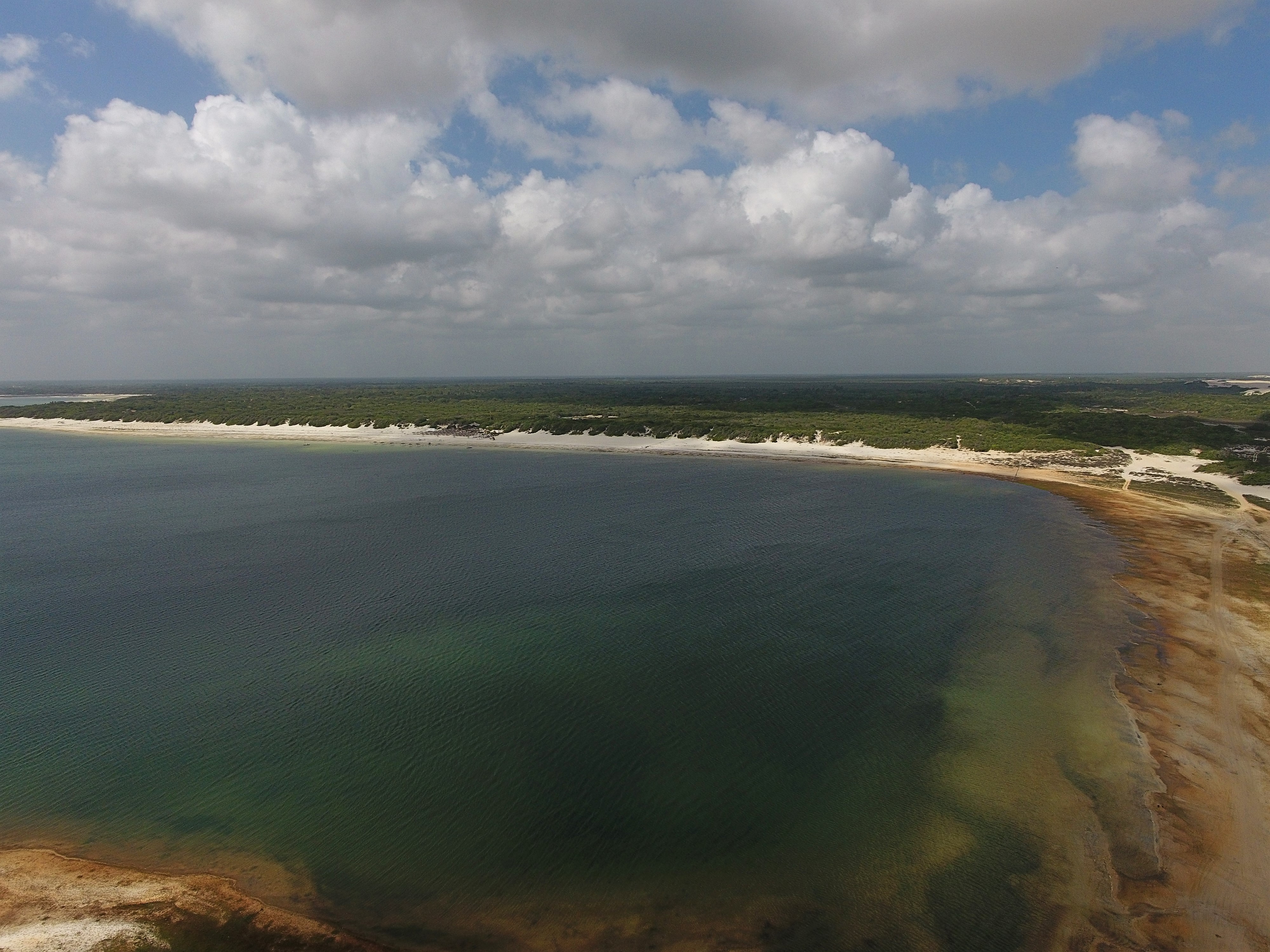 Fotografia da Lagoa do Paraíso tirada de cima. As águas tem um tom azul escuro, quase esverdeado. O céu está coberto com nuvens na cor branca e cinza