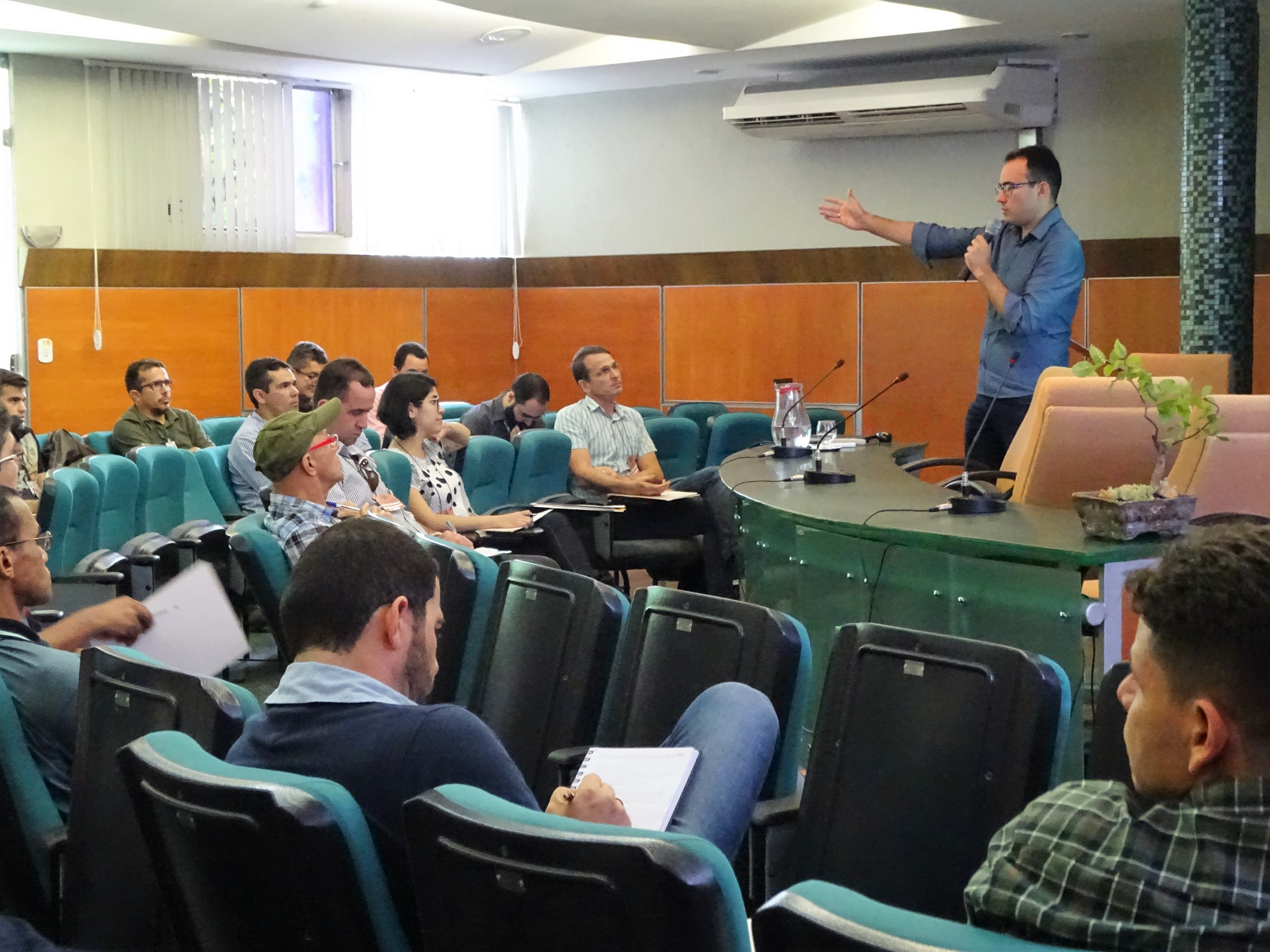 Fotografia realizada durante o seminário. Na imagem, os participantes estão sentados à, nos assentos verdes do auditório da Semace. À direita, em pé atrás da bancada, o superintendente Carlos Alberto Mendes fala ao microfone e gesticula com a mão direita, como se apontasse algo