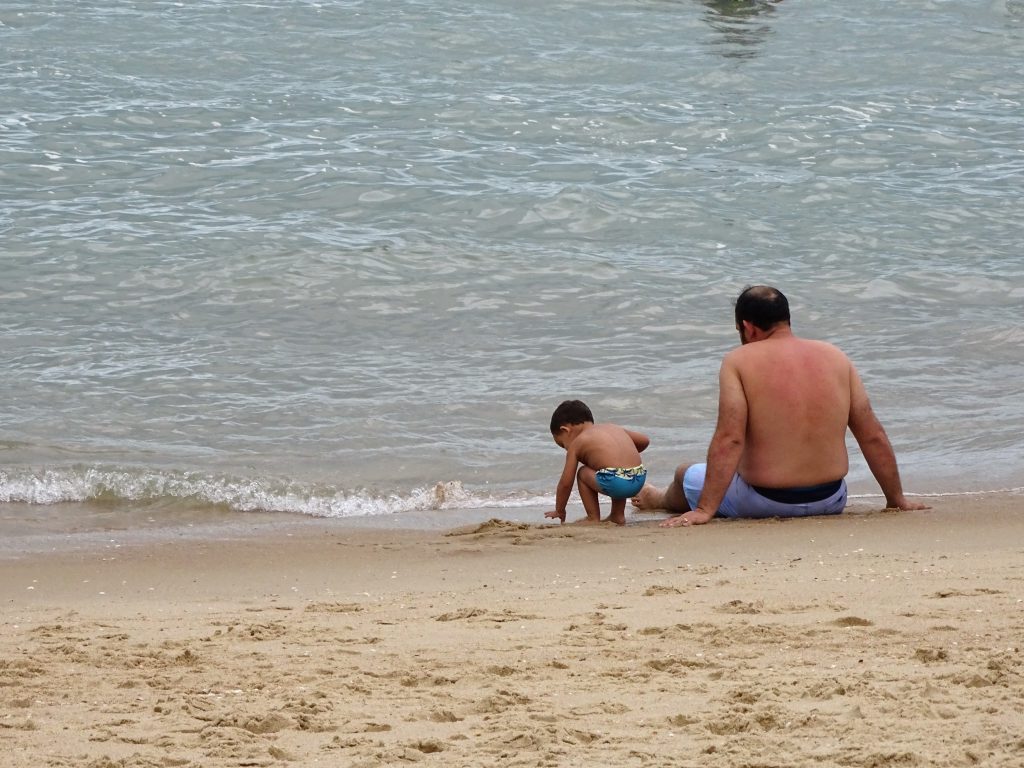 Pai e filho brincam na praia, perto do mar