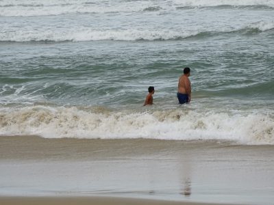 Praia com mar. Pai e filho tomam banho
