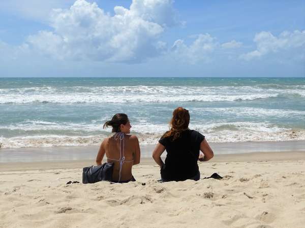 Duas mulheres sentadas na praia, de frente para o mar