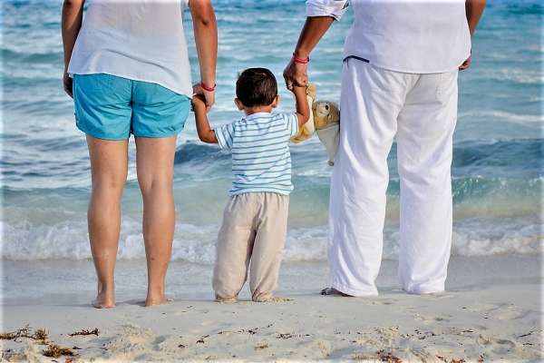 Pais e filho pequeno na praia observam o mar