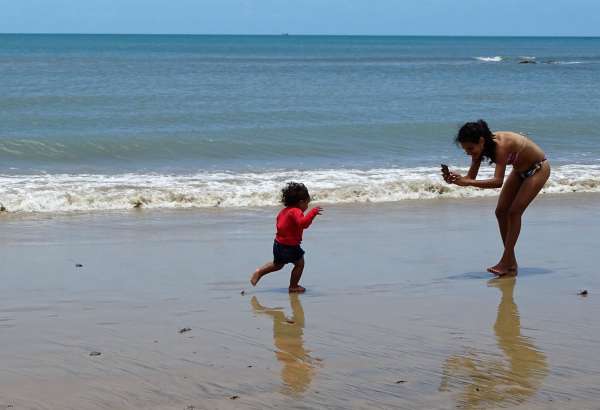 Mulher fotografando criança na praia