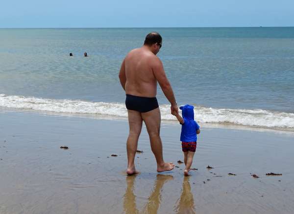 Pai leva filho pela mão para tomar banho de mar
