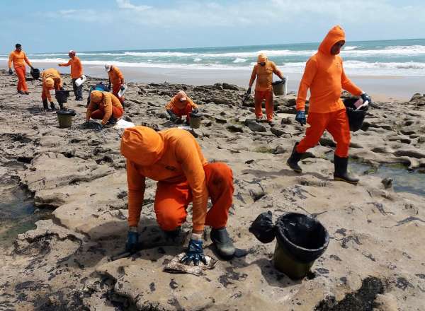 Homens removem óleo das pedras da praia de Sabiaguaba